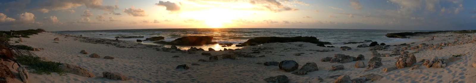 Weites Panorama bei Sonnenaufgang über Felsen und Sand an Cozumels Ostküste.
