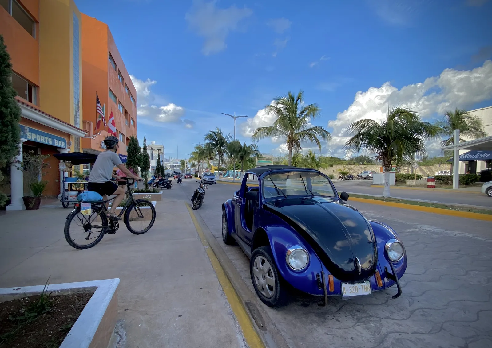 A blue Volkswagen, bicycles and palm-lined buildings on a street in San Miguel de Cozumel.